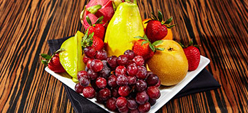 Fruit platter with apples, strawberries, grapes, pears, lemon, and oranges on white ceramic plate