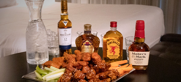 Table with ice water whiskey, Macallan, Crown Royale whiskey, Fireball whiskey, Maker's Mark whiskey, with chicken wings, celery sticks, and carrot sticks